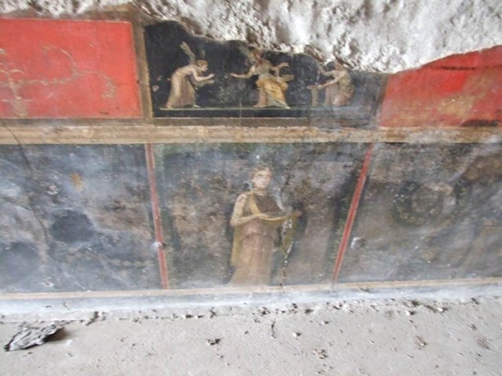 VI.15.1 Pompeii.  December 2006. Room of the Cupids or Cherubs.  Wall painting.  Above is a wall painting of three Psychai gathering flowers.
Below is a female figure or priestess holding implements of sacrifice.
