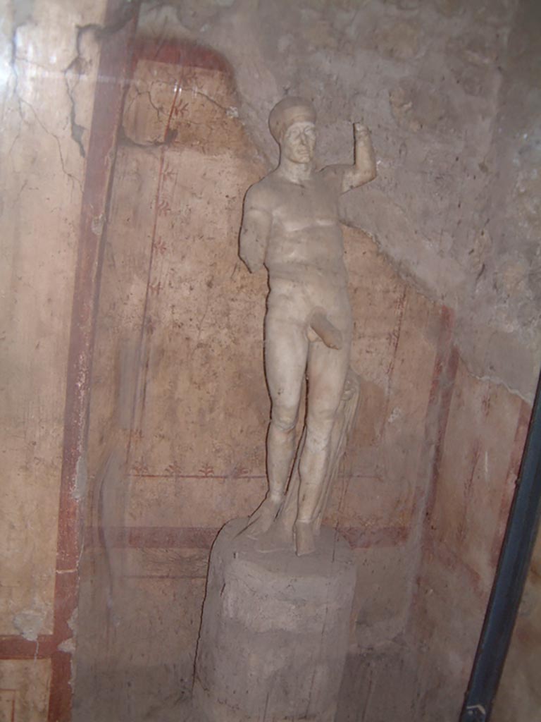 VI.15.1 Pompeii. May 2001. 
The statue of Priapus in bedroom recess in room (x’), used either by servants or as a private brothel?
Photo courtesy of Current Archaeology. 
According to Sogliano –
“In this kitchen, on 14th May 1895, some vases of bronze and terracotta were found, together with other items. 
Also found were two marble statues, both of which without doubt belonged to the peristyle: the first (0.84m high) missing its right arm, its left foot and its right hand, showed Theseus, ……..: 
the second statuette (0.95m high) was found in pieces, and showed Priapus, completely nude……… 
Missing his right forearm and toes: his left arm was found detached from his torso. 
The head, broken into two pieces, the phallus and the pillar were found on 6th August.
The described statuette of Priapus is now preserved in the cubiculum communicating with the kitchen, and decorated with the usual obscene paintings roughly executed.
See Sogliano, A. La Casa dei Vettii in Pompei in Mon. Ant. 1898. (p.269).
