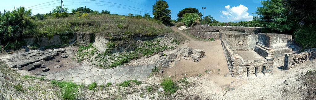 Pompeii Porta Sarno Necropolis. 2019. Panoramic view of excavation site. 
The continuation of the Via dell'Abbondanza, the ancient road from the gate, now blocked by the railway, is to the extreme left running west to east. 
The paved area to the right of the Via dell’Abbondanza is a secondary road leading to the road that runs around the city walls.
Photo courtesy Necropolis of Porta Sarno Research Project.

