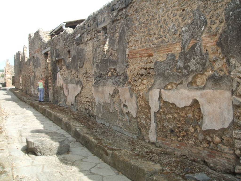 Vicolo di Tesmo looking north past remaining painted plaster on walls outside IX.7.20.
On the exterior wall of IX.7.20, opposite the doorways of IX.2.17/18, a large painted lararium was found.
According to Trendelenburg, this stood out because of the freshness and strength of the colours.
It was divided into two parts, of differing sizes. The upper part was 1.47m wide and the lower part was 4.12m wide.
The upper part showed the two Lares.
In the middle between them was the Genius with cornucopia, dressed in a white tunic holding a patera above a flaming altar. 
Behind the altar was the figure of small tibicen who played the double pipes. 
Suspended above were two garlands and above the garlands appeared the bust of Luna on the left and a bust of Sole on the right. 
The lower part showed a tall altar in the centre and three heads of Medusa. 
Two serpents approached the altar, one from each side.
See Trendelenburg in BdI 1871, pp. 199-200.
See Sogliano, A., 1879. Le pitture murali campane scoverte negli anni 1867-79. Napoli: Giannini. (p.14, No. 33).
See Fröhlich, T., 1991. Lararien und Fassadenbilder in den Vesuvstädten. Mainz: von Zabern. (F65, p. 335)