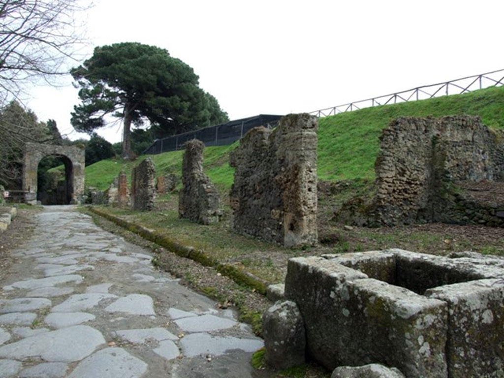 Fountain III.11.1 Pompeii. March 2009. Via di Nola looking east to Nola Gate, taken from outside III.11.1 and fountain.
Eschebach numbers this as III.12.f. CTP rejects this and refers to the insula as being III.11 (A to H). 
The insula is shown on the World of Pompeii maps as III.11.1-7 and a. The fountain is now at III.11.1.
See Eschebach, H., 1983. Pompeii, Herculaneum, Stabiae; Bollettino dell’Associazione Internazionale Amici di Pompei 1, p. 12, Kat. Nr. 10. 
See Van der Poel, H. B., 1986. Corpus Topographicum Pompeianum, Part IIIA. Austin: University of Texas, p. 66 and 85. 
See Dobbins, J. J. and Foss, P. W., 2008. The World of Pompeii. Oxford: Routledge. CD with map.