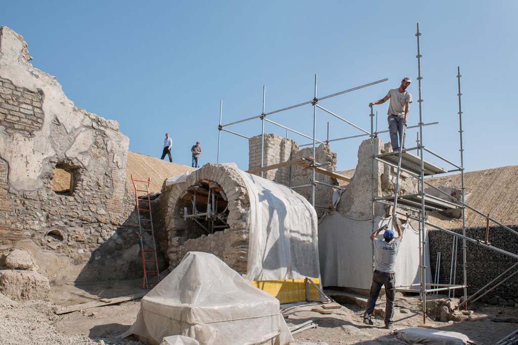 Pompeii Fountain at V.8 during excavation. 
Looking north-east from crossroads on Vicolo delle Nozze d’Argento, towards a small square/open area with water tower at rear, well/cistern with arched roof and fountain (covered). 
The gladiator fresco is on the back of the wall to the right of the water tower and behind the well/cistern.
Fontana di Pompei a V.8 durante lo scavo. Quadrivio con torre d'acqua sul retro, pozzo/cisterna con tetto ad arco e fontana (coperta). 
L'affresco gladiatore si trova sul retro della parete a destra della torre dell'acqua e dietro il pozzo/cisterna.
Photograph © Parco Archeologico di Pompei.