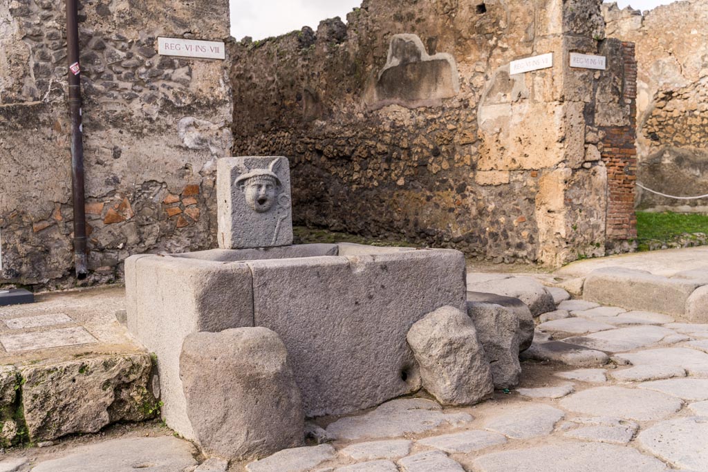 Fountain outside VI.8.24, Pompeii. January 2023. 
Looking north-west from Via di Mercurio towards junction with Vicolo di Mercurio, at rear of fountain. Photo courtesy of Johannes Eber.