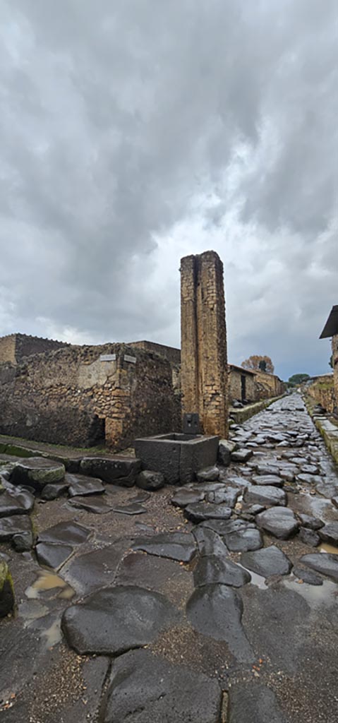 Fountain and water column between VI.16.3 and VI.16.4. 
December 2023. 
Looking north on Via del Vesuvio. Photo courtesy of Miriam Colomer.