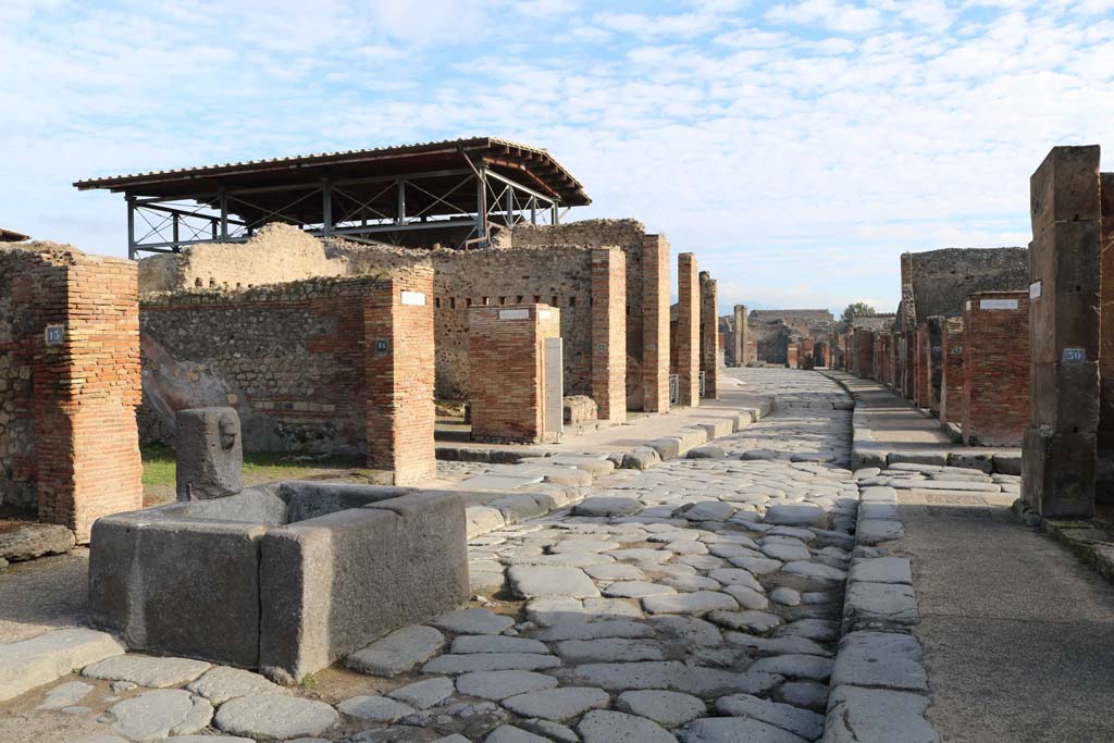 Fountain outside VII.14.13 and VII.14.14 on Via dell’Abbondanza, Pompeii. December 2018. 
Looking east from fountain towards junction of Vicolo del Lupanare, on left, and Via dei Teatri, on right. 
Photo courtesy of Aude Durand.