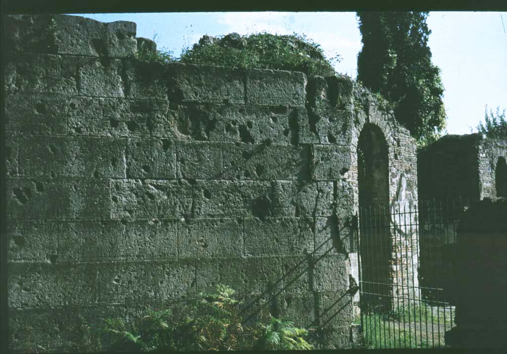 Pompeii Porta Ercolano or Herculaneum Gate east side. Looking south towards city walls.
Photographed 1970-79 by Günther Einhorn, picture courtesy of his son Ralf Einhorn.
See Notizie degli Scavi, 1943, (p.275-294), 
for article entitled “Isolation of the wall between the Vesuvian Gate and Herculaneum Gate.”
(Isolamento della cinta murale fra Porta Vesuvio e Porta Ercolano).
According to Van der Graaff –
“Littered with scars from the Sullan siege, the fourteen-course section still displays some of the highest-quality finished masonry of the entire circuit (Note 75). It is also unique as the only stretch of fortifications composed entirely of tuff – a circumstance reflecting its prominent position next to the gate……….
The resulting effect set the stage for approaching viewers of the architectural character of the city behind the gate.”
See Van der Graaff, I. (2018). The Fortifications of Pompeii and Ancient Italy. Routledge, (p.65 and Note 75).