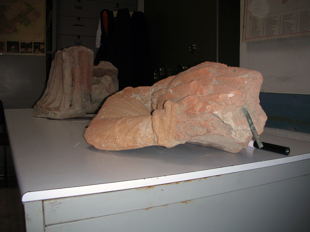 Pompeii Ports Marina. The fragments of the statue of Minerva in 2010.
Photo courtesy of Ivo van der Graaff.
According to Van der Graaff, the excavation report of 1861 describes the recovery of three large terracotta statue fragments and two smaller pieces of a hand associated with the shrine. Hermann Von Rohden reunited the fragments in a drawing published in 1880, but they subsequently vanished into obscurity and were considered lost. In the summer of 2010, some research and the aid of the site director at Pompeii, Dott.ssa Grete Stefani, led to the rediscovery of the fragments, which were stored in a corner of one of the storerooms in Pompeii. Although somewhat battered, the pieces unmistakably join into the Von Rohden reconstruction. The figure stands on her left leg in a gentle contrapposto pose with her right hand resting on her hip. She wears a sleeveless chiton, and a chlamys draped over her right shoulder and arm. The head is gone as is almost the entirety of her left side above the knee. A stylized rock next to her left foot preserves the remnant of a shield that once stood next to her leg, indicating that the statue represents the same Minerva present at the other Pompeian gates. The fragmentary state makes any dating based on stylistic grounds problematic. The niche in its current version is almost certainly associated with postcolonial refurbishment of the gate. However, given the continuity of cult recovered at the Porta Stabia, the statue may be a relic of an earlier phase. The fact that excavators recovered only about half of the statue indicates that already in antiquity it was an important artifact. The context indicates that the statue broke at some point before the eruption. Although broken and battered, the remaining pieces were put back into place where they continued to evoke her presence.
See Van der Graaff, I., 2019. The Fortifications of Pompeii and Ancient Italy. Abingdon, Oxon: Routledge, pp. 209-211, pl. 30.