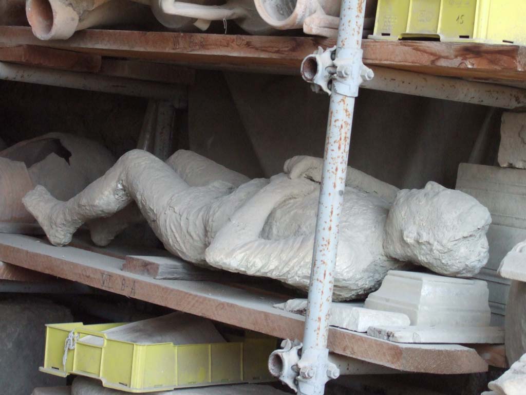 VII.7.29 Pompeii. May 2006. Forum Granary store. Plaster cast of body, known as victim number 13. 
Garcia y Garcia described a mature man, already old, but perhaps still vigorous, fallen on his back, wrapped in a wide cape, with hands on his chest and with slightly drawn up legs. 
He had a fine aquiline nose and a smile was on his lips. On the right leg was a circular ring that denoted a slave. 
This plaster cast was obtained outside the Stabian Gate on the 11th of October 1889, at approximately 10 metres if you are exiting and turn to the right. 
A plaster cast was also made of a woman who was found next to this man.
See Garcia y Garcia, L., 2006. Danni di guerra a Pompei. Rome: L’Erma di Bretschneider. (p. 193-4, Figg. 451-3).
According to Dwyer, this plaster cast was of victim number 14.
See Dwyer, E., 2010. Pompeii’s Living Statues. Univ. of Michigan Press: (p.103)