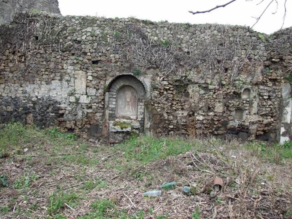 VII.11.14 Pompeii. March 2009. Garden “C”, west wall.
According to Boyce –
Against the west wall of the large open area in the south-west corner, stands a lararium. 
Above a rectangular podium (0.95 by 0.60, h.105) a projecting arch was built against the back wall, thus forming a niche (h.1.02, w.0.70, d.0.32).
The front part of the upper surface of the podium served as an altar for sacrifices before the figures painted on the walls of the niche, on the front side of the podium was a step.
On the rear wall of the niche are painted Jupiter and the Genius, each pouring a libation upon the blazing cylindrical altar between them.
Jupiter stands on the right, on the left is the Genius.
To the right and left on the wall outside the niche were the poorly preserved figures of the Lares.
The side walls and the vaulted ceiling of the niche were decorated with leafy boughs.
The exterior of the structure was coated with stucco painted in several different colours.
See Boyce G. K., 1937. Corpus of the Lararia of Pompeii. Rome: MAAR 14. (p.69, no.310 with Pl.14,1)