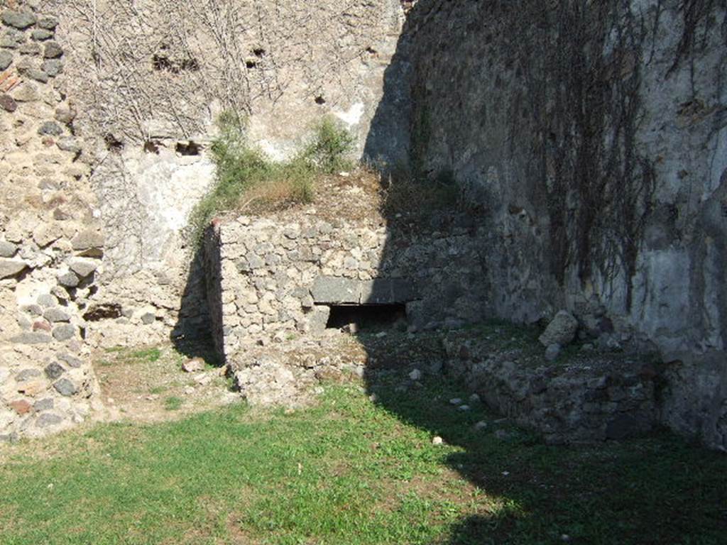 VII.12.7 Pompeii. September 2005. Looking east towards oven in south-east corner of rear area.
According to Boyce, on the south wall of the room with the oven was a large lararium painting (2.0 square).
In the centre was a blazing tripod, with the Genius to the right of it.
On each side was a wreathed Lar. 
To the left of this group stood Vesta, at her side was an ass with a bell around its neck.
On the right of the group stood Mercury.
In the lower zone, marked off from the upper by a brownish stripe, were the two serpents.
They were approaching a gold-coloured altar, on top of which was a white shallow dish containing a blazing fire.
In the fire was an egg and several fruits – a date, a pomegranate and a medlar.
See Boyce G. K., 1937. Corpus of the Lararia of Pompeii. Rome: MAAR 14. (p.70, no.313). 
See Helbig, W., 1868. Wandgemälde der vom Vesuv verschütteten Städte Campaniens. Leipzig: Breitkopf und Härtel. (68)
According to BdI, this was the first time that Mercury appeared associated with the Lares, in Pompeii.
See Bullettino dell’Instituto di Corrispondenza Archeologica (DAIR), 1864, p.114-115 (described as Casa II.)