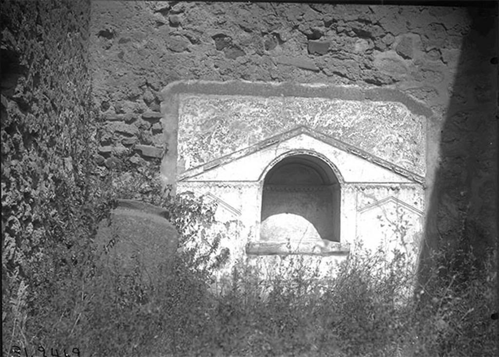 VII.15.8 Pompeii, 1931. Looking towards niche in north wall of garden area. 
DAIR 31.2462. Photo © Deutsches Archäologisches Institut, Abteilung Rom, Arkiv. 
According to Boyce –
in the centre of the north wall of the garden area near the floor, was an arched niche (h.0.59, w.0.53, d.0.26, h. above floor 0.50).
The wall around it was covered with a rectangular panel (h.1.40, w.1.65) of white stucco.
On this was an aedicula façade which was marked off with yellow and violet lines in low relief.
The work was delicately executed but somewhat irregular.
His reference Bull. Inst., 1874, 65.
See Boyce G. K., 1937. Corpus of the Lararia of Pompeii. Rome: MAAR 14. (p.72, no.332, Pl. 6,2) 
See Giacobello, F., 2008. Larari Pompeiani: Iconografia e culto dei Lari in ambito domestico. Milano: LED Edizioni, (p.281 no.V69)