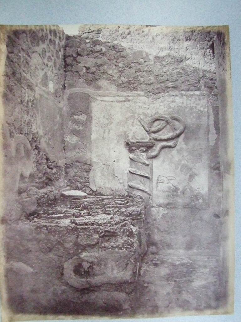 VII.15.13 Pompeii.  Kitchen with altar and Genius Lar relief on east wall.
Old undated photograph courtesy of the Society of Antiquaries, Fox Collection. A Lar can be made out in the top left hand corner, and a hog’s head on the right side of the altar.