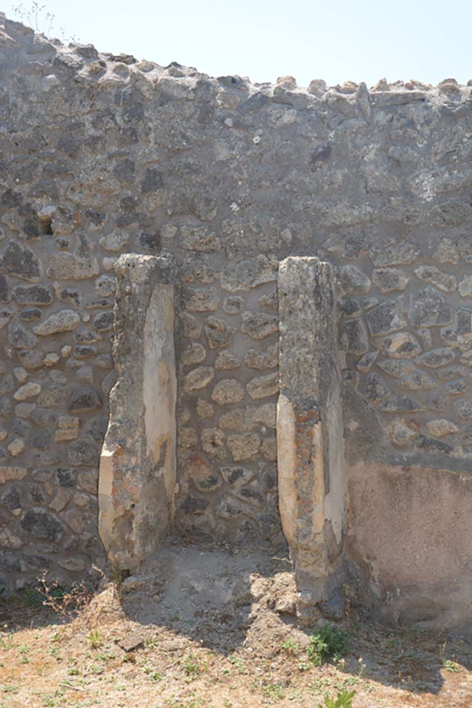 IX.2.27 Pompeii. July 2017. Looking towards west wall of peristyle, with remains of shrine. 
Foto Annette Haug, ERC Grant 681269 DÉCOR.
According to Boyce, -
Above a low podium (1.10 by 0.70, h.0.40) two enclosing walls (h. as far as preserved 1.30) built against the wall of the room form a rectangular niche (w.0.60, d.0.50) above a low podium, but none of the floor was preserved. 
The inside walls are painted blue with red borders. 
On the ground in front of the shrine stood a square masonry altar.
See Boyce G. K., 1937. Corpus of the Lararia of Pompeii. Rome: MAAR 14. (p. 82, no. 405)
Giacobello described this as an Aedicula lararium. 
See Giacobello, F., 2008. Larari Pompeiani: Iconografia e culto dei Lari in ambito domestico. Milano: LED Edizioni, (p.284 no.V77)