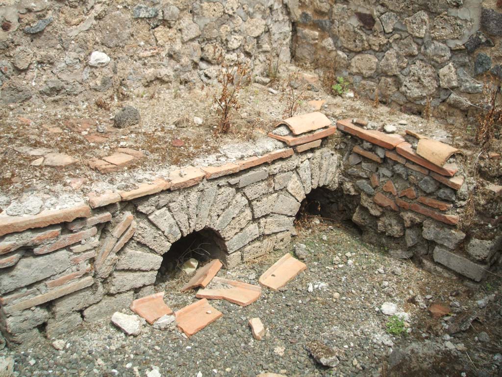 IX.5.14 Pompeii. May 2005.  Room “q”, kitchen.
Looking north-east towards hearth in kitchen (room “q”), on south side of peristyle, in servants’ area.
According to Boyce, on the south wall of this kitchen, was a fragmentary lararium painting.
Boyce said that Mau thought this kitchen was reserved for the use of the members of the household.
See Boyce G. K., 1937. Corpus of the Lararia of Pompeii. Rome: MAAR 14. (p.86, no.426).  
See Sogliano, A., 1879. Le pitture murali campane scoverte negli anni 1867-79. Napoli: (p.19, no.69)