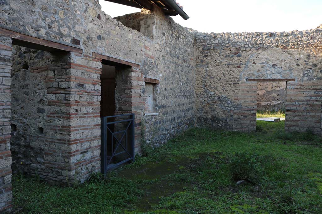 IX.5.16 Pompeii. December 2018. 
Looking north across atrium a’ from entrance doorway, on right is the doorway into the atrium “b” of IX.5.14.
On the left (west) side of atrium a’, on the left, is the doorway to kitchen and latrine e’.
Centre left, is the doorway to cubiculum f’.  Photo courtesy of Aude Durand.
According to Boyce, on the south wall of the kitchen was a large rectangular panel (h.1.0 w.2.0) of white stucco.
On it were painted two yellow serpents with red crest and beards. 
These were on either side of a tile embedded and projecting from the wall.
A fire was painted on the wall above the tile.
The background was painted with plants, and across the top were two painted garlands.
On each of the garlands was a painted bird.
See Boyce, G. K., 1937. Corpus of the Lararia of Pompeii. Rome: MAAR 14.  (p. 86, no. 425)
See Giacobello, F., 2008. Larari Pompeiani: Iconografia e culto dei Lari in ambito domestico. Milano: LED Edizioni, (p.208, no.102)