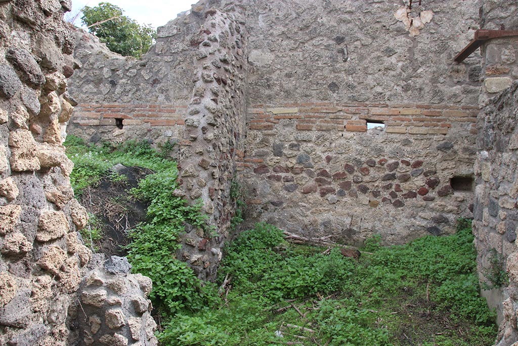 IX.7.16 Pompeii. October 2024. 
Room “d”, on south side of room 3, on right, looking south through site of wall and doorway into kitchen, no longer in situ. 
On the left would be a doorway into room 6. Photo courtesy of Klaus Heese.
According to Boyce –
“In the kitchen, which is entered through the first room on the right of the atrium, on the north wall to the right of the entrance and on the west wall, is the lararium painting (h.1.50, w. on north wall 0.60, on the west wall 1.94): on the right of an altar stands the Genius in the usual attire, pouring a libation from a patera; on the left is the lower part of the figure of the tibicen and behind him stands a camillus wearing white tunic and carrying in his left hand, a shallow dish, taeniae in the right hand. Behind the Genius the popa, wearing a crown of leaves, holds a knife to the throat of a hog adorned with a red band around its belly. On each side of this group of four is a Lar in the usual attire. In the lower zone two yellow serpents, each with red crest, are confronted at an altar. The painting thus described is all on the west wall of the room. On the north wall are painted the following kitchen objects (from top to bottom): a hearth, an uncertain object – perhaps the fire-wood for the hearth – a hog’s head, a pot on a fire.
Traces of the older lararium painting, not entirely covered over by the later, are to be seen on the west wall, where the figure of a Lar can be made out on the left side.”
See Boyce G. K., 1937. Corpus of the Lararia of Pompeii. Rome: MAAR 14. (p. 87, no. 436) 
and Boyce gives the reference Bullettino dell’Instituto di Corrispondenza Archeologica (DAIR), 1883, 145.