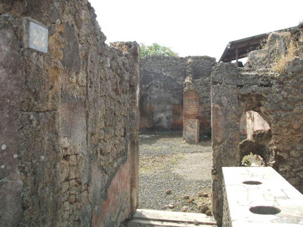 IX.7.24 Pompeii. May 2005. Looking south across thermopolium (a) to doorway to atrium (2) of IX.7.25
The doorway between the shop and the atrium had the threshold of a dark marble and was closed by two battens.  
See Mau in Bullettino dell’Instituto di Corrispondenza Archeologica (DAIR), 1882, (p.148)
According to Boyce, in the south wall was a vaulted niche (h.0.44, w.0.44, d.0.51, h. above floor 1.20).
Its inside walls were coated with orange-coloured stucco.
Above the niche was a painting (h.0.30, w.0.73) of the two serpents confronting at an altar.
He references – Not. Scavi, 1880, 395; Bull. Inst., 1882, 148.
See Boyce G. K., 1937. Corpus of the Lararia of Pompeii. Rome: MAAR 14. (p.88 no.443)