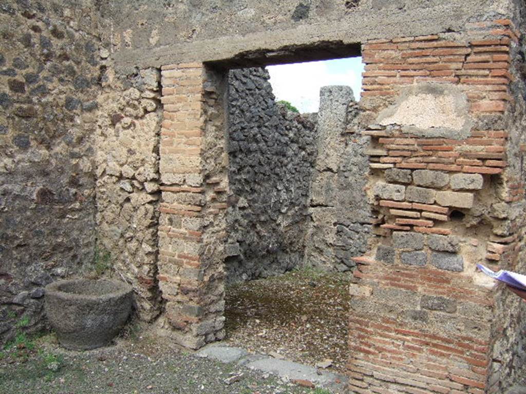 IX.9.6 Pompeii. May 2006. Doorway to cubiculum in north-west corner of atrium.
According to NdS, the doorway to this room was made narrower by the addition of a pilaster formed by rows of masonry bricks and tufa cut in a similar style, on its left. When found, this doorway was furnished with a door, the imprint of which could be seen at the time of excavation, but it could not be saved. The room had a rough signinum floor, and rustic walls. In the west wall was a semicircular niche, plastered entirely in white stucco studded with coloured specks, which could have been flowers. In this room, some amphorae were found (see NdS, 1887, p.561) containing lime. In the rustic plaster, on the pilaster between the entrance corridor and the doorway to the room (right in picture above), graffiti were found. They read –
IVCVNDVS        and          QVOIVS
 VIINVS                                LABORE
 VITALIS
See Notizie degli Scavi, 1889, p.123.