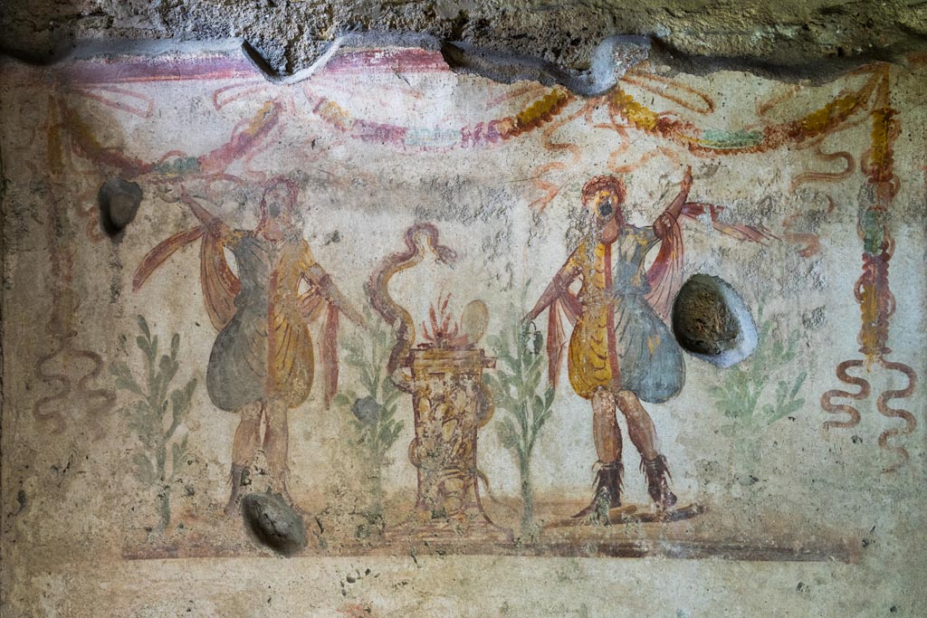 IX.9.c Pompeii. March 2023. 
Detail of two Lares either side of a round altar which has a serpent winding around it. Photo courtesy of Johannes Eber.