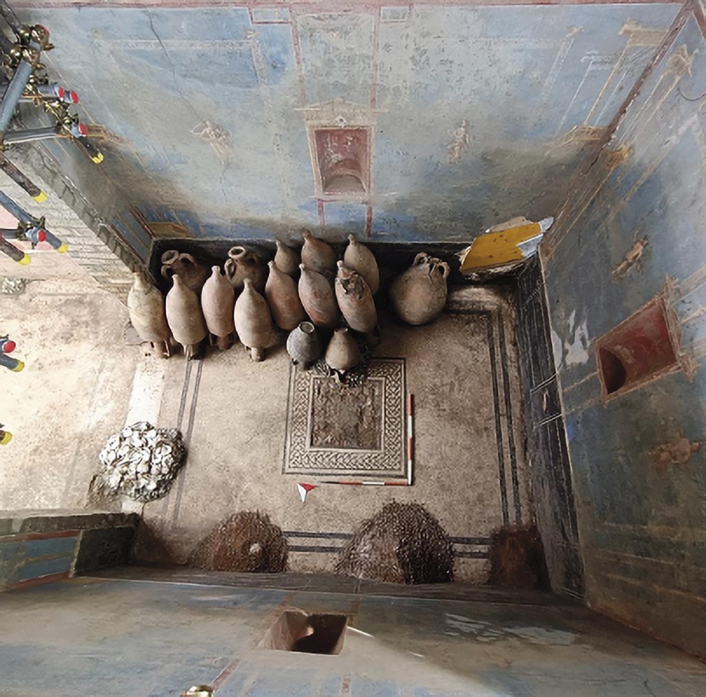 IX.10 Pompeii. House on west side of insula, south of IX.10.1. June 2024. Sacrarium room 32 with blue decoration, showing identical niches in red on three walls.
Once the stratigraphic sequence was removed, two piles of cocciopesto of different grain sizes and a third pile with a mixture of lime, aggregates and cocciopesto were brought to light (fig. 6). The accumulations of pozzolana and cocciopesto can be traced back to the construction activities present in the house, in particular the room, originally a finely decorated chapel, was used shortly before the eruption as a deposit for amphorae and a place to store building materials.
It should therefore come as no surprise that the sacrarium itself, at the time of the eruption, was transformed into a depository for amphorae and building materials: even when it was in operation, it was not a place with an exclusive sacral function; this distinguishes the sacraria from the lararia, which indeed retained their ritual centrality for longer, probably because they were directly linked to the exercise of the pater familias' power (cf. Van Andringa 2009).
Download PAP 15-E-Journal-Sacrario-Regio-IX.pdf, Fig. 6, p. 4.
The newly resurfaced room presents characteristic elements that refer to the architectural articulation of similar contexts and in particular the presence of niches embedded in the south, east and west walls. If the presence of niches in itself is not an exclusive characteristic of sacred environments, the monumentality that they take on in this context, especially in relation to the fusion with a decorative system, designed in relation to the presence of these elements, make the new discovery particularly interest. In the last phase of the domus' life, this room was also used as a storage for containers, with the usual tally notes written on the east jamb after the entrance, and to accumulate building materials. It was then explored between the 18th and 19th centuries through a tunnel to recover part of the furnishings and perhaps the polychrome marble emblem placed in the center of the floor mosaic. These are perhaps the reasons why the cult images were not found inside the niches, either taken in ancient times to be stored while awaiting the end of the building works on the house or taken away during eighteenth-nineteenth century explorations.
See PAP 15-E-Journal-Sacrario-Regio-IX.pdf, p. 5.
Photograph © Parco Archeologico di Pompei.