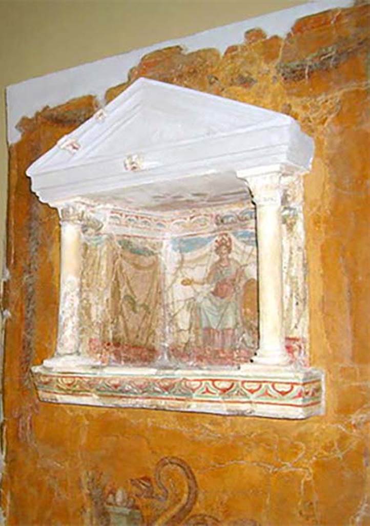 97. Gragnano, Villa rustica in Località Carmiano, Villa A. Lararium niche. 
From dividing pilaster between kitchen room 4 and room 2. 
Lararium in stucco found inserted in a yellow painted wall.
The lararium had a triangular pediment supported by two Corinthian columns.
The painting at the rear showed an enthroned Minerva with breastplate, helmet, shield, lance in the left hand and gilded/golden plate in the right.