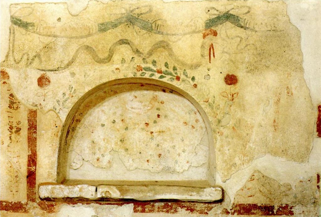 Scafati. Villa rustica in proprietà Rosa Buccino via Tenente Jorio. Piccolo larario in forma di nicchia semicircolare.
In alto si trova una ghirlanda di nastri. Sopra la parte superiore della nicchia si trova un serpente che si muove verso destra.
Intorno al bordo della nicchia c'è un bordo di una pianta con fiori rossi e un fiore rosso più grande su ogni lato in alto. 
L'interno della nicchia presenta un motivo rosso e verde su sfondo bianco.
A destra si trovano quelle che potrebbero essere le gambe di una figura.
Scafati. Villa rustica in proprietà Rosa Buccino via Tenente Jorio. Small lararium in the form of a semicircular niche.
At the top is a garland of ribbons. Above the top of the niche is a serpent moving to the right.
Around the rim of the niche is border of a plant with red flowers and a larger red flower is on each side at the top. 
The interior of the niche has a red and green pattern on a white background.
To the right are what may be the legs of a figure.
Vedi/See Conticello de' Spagnolis, M., 1994. Il Pons Sarni di Scafati e la via Nuceria-Pompeios, Soprintendenza Archeologica di Pompei Monografie, 08, p. 31, fig. 19.