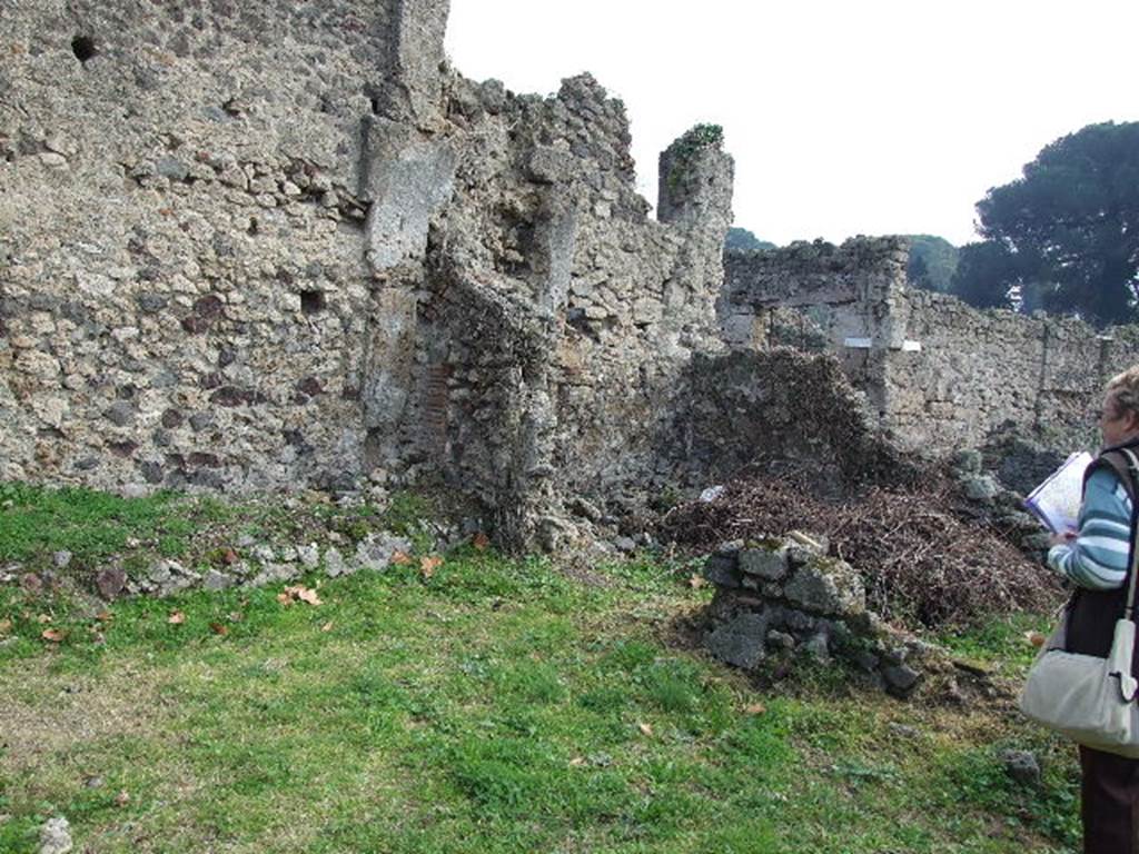 I.2.3 Pompeii. December 2006. Looking across the garden area, towards the remains of the two rooms in the south-east corner. According to Fiorelli, on the opposite side of the garden from the vestibule and bedroom, was a storeroom and a room uniquely used for the sacred domestic Gods (Sacellum). A brick altar was in the middle, on which was painted a cock. The image of the Genius was painted on the wall pouring a libation onto the altar. Nearby was a large serpent, plants, and it was surmounted by garlands with small birds.
See Pappalardo, U., 2001. La Descrizione di Pompei per Giuseppe Fiorelli (1875). Napoli: Massa Editore. (p.34).
According to Boyce, on the south side of the Viridarium were two small adjoining rooms. One was a storeroom and the other, according to Fiorelli, was devoted only to the service of the domestic cult.   In the centre of the room entered from the first door stood a masonry altar, on which was painted a cock.   On the south wall a panel of white stucco was marked off with red stripes and within it was the Lararium painting.
The Genius poured a libation upon an altar, towards which a large serpent moved, moving through plants. Across the top were three small festoons, on each of which perched a little bird.
See Boyce G. K., 1937. Corpus of the Lararia of Pompeii. Rome: MAAR 14.  (p.21 No.4)