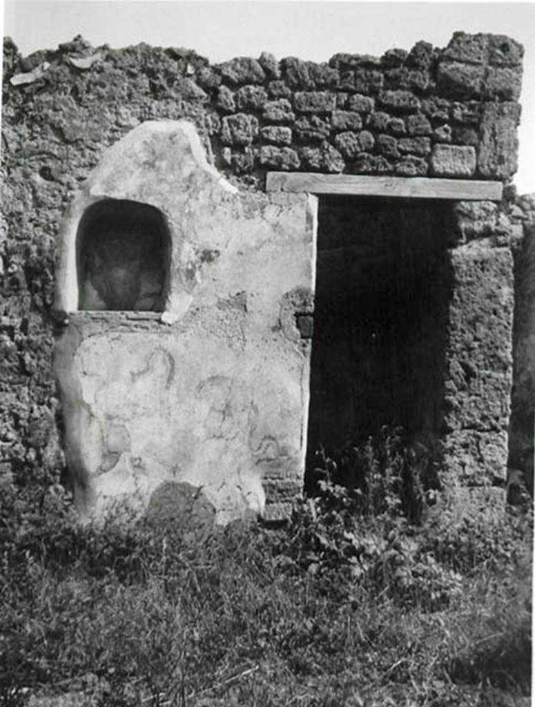 I.2.24 Pompeii. 1935 photo taken by Tatiana Warscher.
Looking towards south wall of atrium, with niche and doorway to understairs area.
See Warscher T., 1935. Codex Topographicus Pompeianus: Regio I.2. (no.45), Rome: DAIR, whose copyright it remains.
According to Boyce, on the south side of the atrium was the lararium.
Above an arched niche (h.0.60, w.0.52, d.0.23, h. above floor 1.35) was painted a cylindrical altar (tripod according to Fiorelli) with a Genius pouring a libation.
Standing beside him was the tibicen and to the left was a Lar. The Lar on the right was not preserved.
Below the niche were the two serpents.
On the wall on each side of the niche was painted a large dog?
The one on the left was poorly preserved but was seen to be lying down, while the one on the right was opening his mouth wide.
From the hindquarters of this second dog there projected horizontally the upper half of the body of a man.
See Boyce G. K., 1937. Corpus of the Lararia of Pompeii. Rome: MAAR 14. (p.23, no.16 and Pl.2,2) 
See Sogliano, A., 1879. Le pitture murali campane scoverte negli anni 1867-79. Napoli: Giannini. (p.17, no.46).