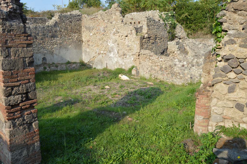 I.2.24 Pompeii. October 2017. Looking towards the north and east walls of the peristyle.  
Foto Taylor Lauritsen, ERC Grant 681269 DÉCOR.
According to Boyce –
In the east wall of the peristyle, above one of the beds of a masonry triclinium, is a niche, described by Fiorelli as a sacrario, more fully by Mau as “un aedicula, una base, cioe, con una piccola tavola, che sta in un specie di nicchia coperta a volta, e probabilmente conteneva un’idolo”. 
There remains now only the solid base (0.40 by 0.32, h.0.65) and on the wall above it the marks left by a vaulted structure which rested on the base.
He quotes references – Bull. Inst., 1874, 262; Fiorelli, Descr., 47.