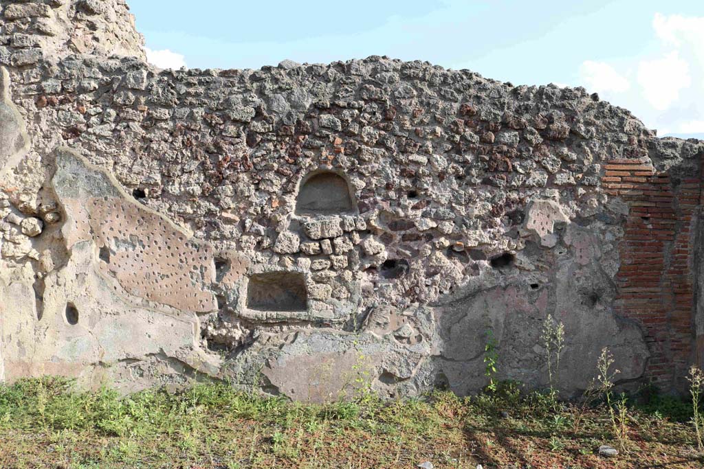 I.4.15/16 Pompeii. September 2018. South wall of shop with two doorways. Photo courtesy of Aude Durand.
According to Boyce, either or both of these could have been lararia. One is 0.50 higher than the other.
The upper niche (h.0.35, w.0.45, d.0.20), was arched and had its walls coated with red stucco.
The lower niche (h.0.30, w.0.50, d.0.27, h. above floor 0.80) having a rectangular opening combined with a back wall which curved from back to front. Its walls were coated with white stucco decorated with painted red dots, to represent flowers.
See Boyce G. K., 1937. Corpus of the Lararia of Pompeii. Rome: MAAR 14. (p.25, no.32).