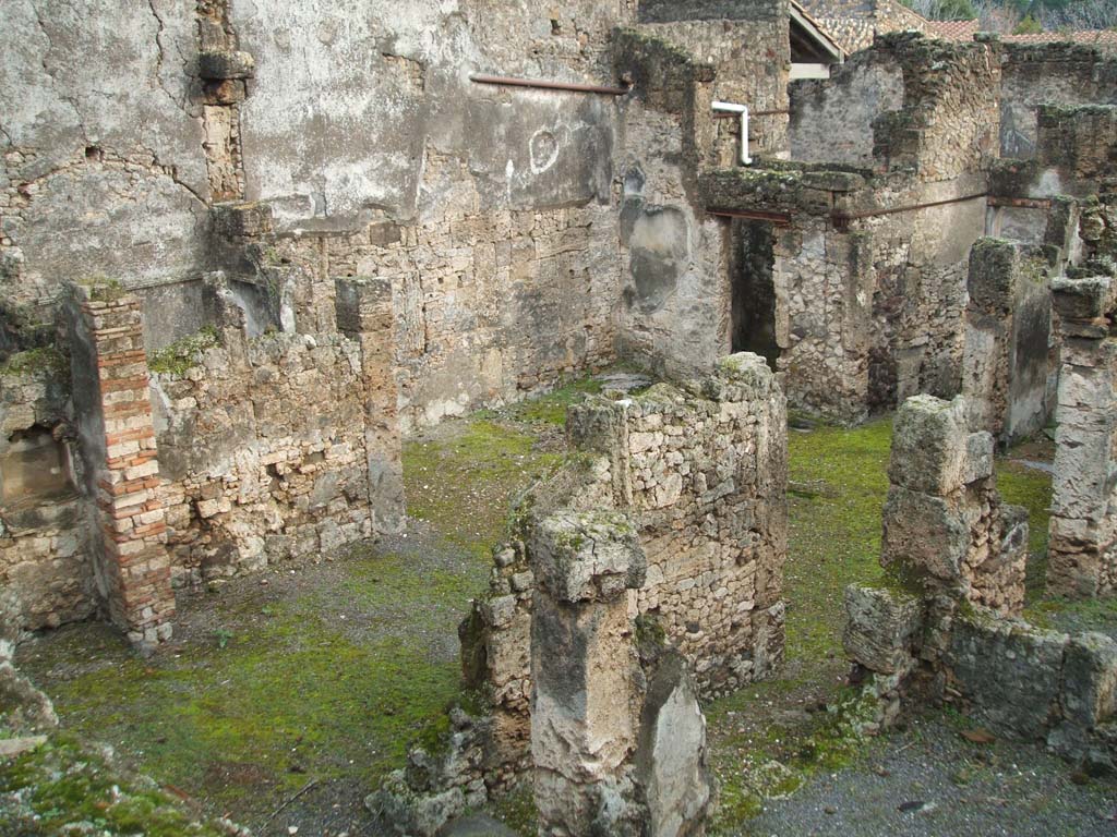 I.6.13 Pompeii. December 2004. Tablinum, atrium and east side looking south-east photo taken from rear of I.6.11. 
Behind the east wall of the tablinum, on left, would be the cubiculum (5) in NE corner of atrium.
Room 7 with doorway to corridor “e” is on the lower right, the corridor “e” is on the west side of the tablinum.
The remains of a lararium niche are on left of picture, in garden area behind tablinum.
According to Boyce –
“In the east wall of the garden is an arched niche (height 0.40, width 0.60, depth 0.27, height above the floor 1.30).
This was referred to in the report as “un modesto larario”.
See Boyce G. K., 1937. Corpus of the Lararia of Pompeii. Rome: MAAR 14. (p. 25, no.38) 
He quotes reference Not. Scavi, 1929, p.434.