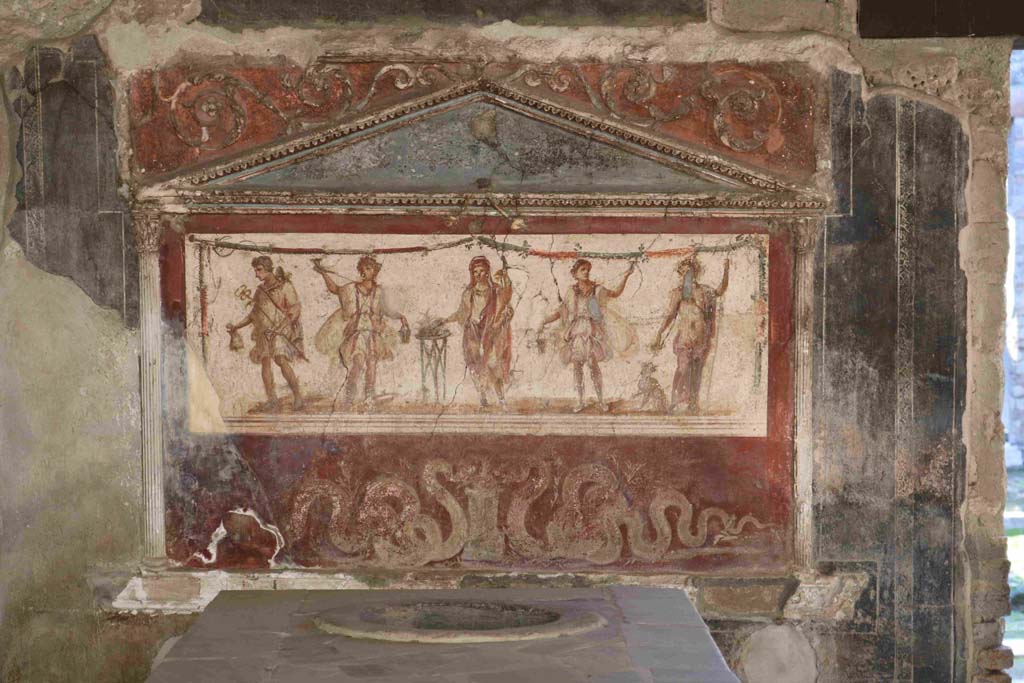 I.8.8 Pompeii. December 2018.Lararium on south wall. Photo courtesy of Aude Durand.
The central figure is the Genius of the household next to a three-legged altar.  
On either side of him are the two Lares. On the left side is Mercury with his money bag.  
On the right side is Bacchus with his panther drinking from a cup held in his right hand.  
Underneath are two serpents approaching a round altar.  
See Fröhlich, T., 1991, Lararien und Fassadenbilder in den Vesuvstädten.  Mainz: von Zabern. (L8: p.252).