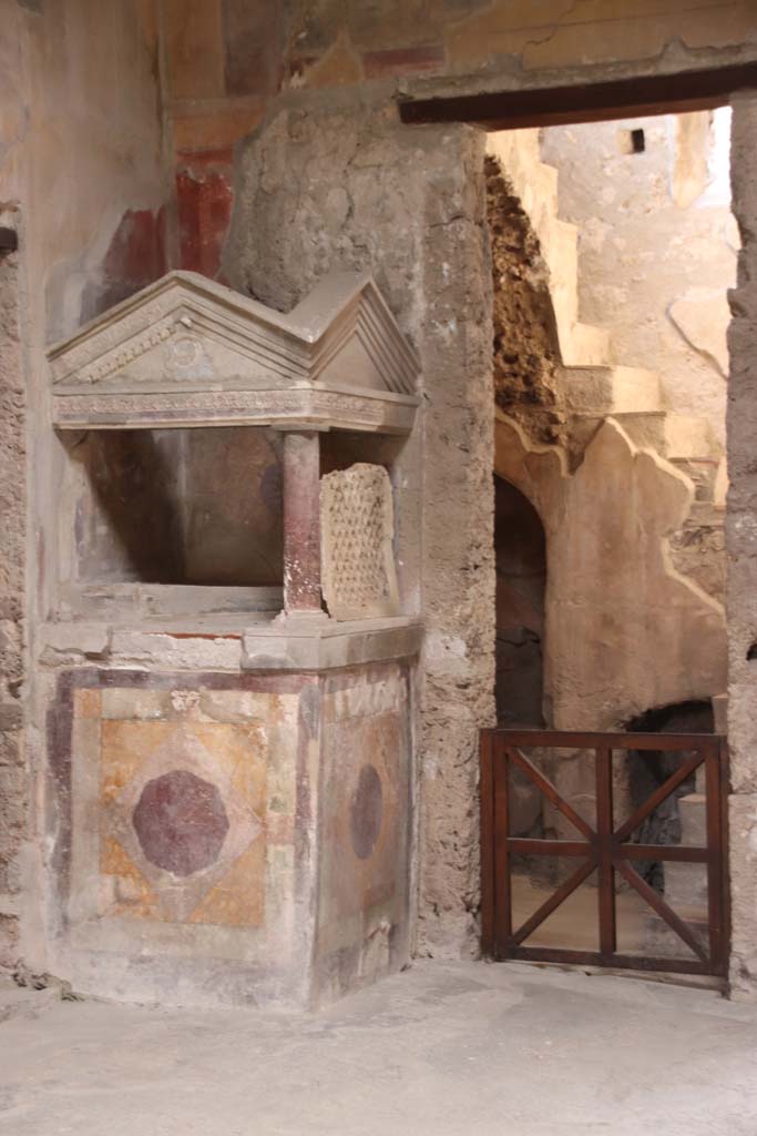 I.10.4 Pompeii. September 2021. 
Looking towards north-west corner of atrium, the lararium and doorway to room 2. 
Photo courtesy of Klaus Heese.
According to Boyce –
A masonry podium (1.08 square, h.1.35) is built into the corner, and above it rises a little temple, formed by a single column at the one free corner of the podium, supporting a roof of two pediments. ………..
See Boyce G. K., 1937. Corpus of the Lararia of Pompeii. Rome: MAAR 14. (p.27-28, no.48).