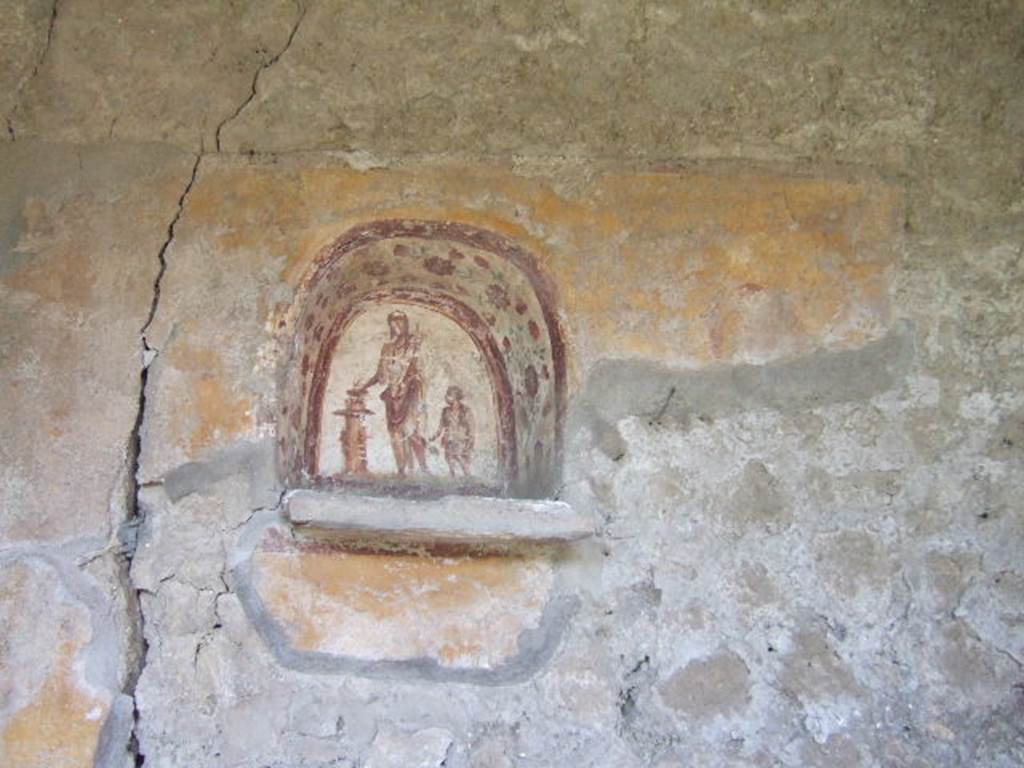 I.17.4 Pompeii. May 2006. Lararium niche on west wall of peristyle garden.  
A genius is making an offering at a round altar. A small camillus is to his left.
The side walls are painted with red flowers possibly roses.
On the yellow-coloured wall outside the niche, a colour trail is visible on the right, which perhaps belongs to a big snake. A paint ridge above the niche may perhaps be interpreted as a garland.
See Fröhlich, T., 1991. Lararien und Fassadenbilder in den Vesuvstädten. Mainz: von Zabern, L37, p. 264, taf. 9,1.