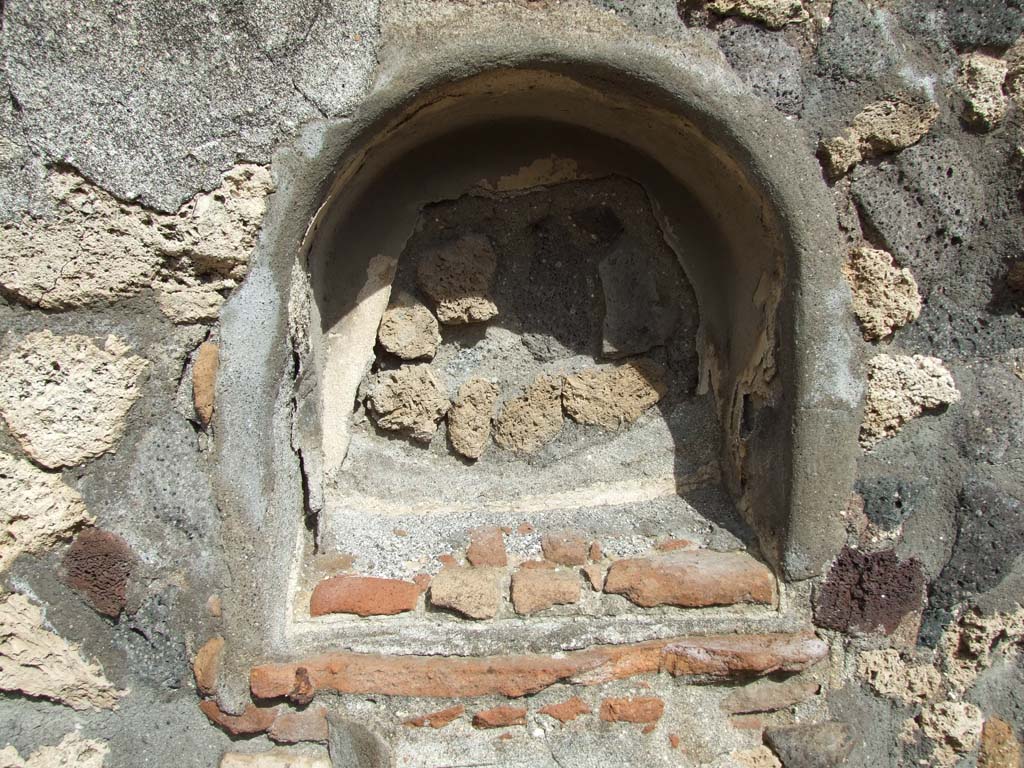 V.1.7 Pompeii. March 2009. Niche on east wall of the peristyle.
According to Boyce, the niche was coated with white stucco and in its floor were three holes for statuettes.
It used to have several iron nails driven into the wall beside the niche at the level of its floor.
Perhaps this was to hold in place an ornamental cornice of wood, as suggested by Mau.
See Boyce G. K., 1937. Corpus of the Lararia of Pompeii. Rome: MAAR 14. (p.32)