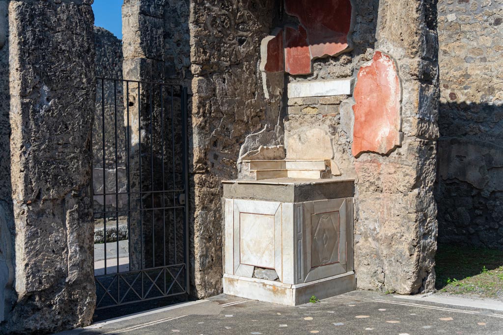 V.1.26 Pompeii. October 2023. Room “b”, north-west corner of atrium with marble lararium. Photo courtesy of Johannes Eber.
According to Boyce –
A high podium (0.96 by 0.86, h. 1.13) is built into the corner and its two free sides are veneered with slabs of greyish marble.
Upon this base must have been erected an aedicula, its roof supported by three wooden pilasters or columns, the marks of the bases of which are still visible on the top of the podium. ………
See Boyce G. K., 1937. Corpus of the Lararia of Pompeii. Rome: MAAR 14. (p.33, no.80).
See Giacobello, F., 2008. Larari Pompeiani: Iconografia e culto dei Lari in ambito domestico. Milano: LED Edizioni, (p.236, no.A10)