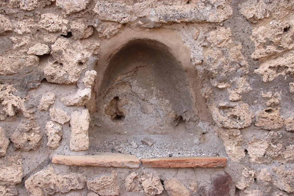 V.2.9 Pompeii. October 2022. Small niche lararium on west wall of shop-room. Photo courtesy of Klaus Heese.
According to Boyce –
this arched niche (approximate measurements h.0.38, w.0.40, d.0.25, height above floor 1.20) was described by Sogliano as la nicchietta dei Penati, in Not. Scavi, 1896, 437.
See Boyce G. K., 1937. Corpus of the Lararia of Pompeii. Rome: MAAR 14. (p.34, no.90).