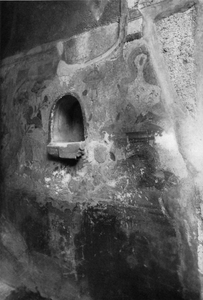 V.2.h Pompeii. c.1930s. In the east wall of the entrance fauces ‘a’ an arched niche can be seen.
According to Boyce, this had a projecting floor and its walls were covered with white stucco.
It was outlined, inside and outside, with red stripes.
The wall beside the niche was painted with the serpents.
To the right of, and below the niche, was painted an unusual altar, resembling a brazier of bronze (see note below*).
Its upper surface was circular and had two handles at the sides.
One of the huge serpents had its body coiled around this altar and was raising its head to the offerings.
The second serpent was painted on the wall to the left of the niche and was raising its head to the niche rather than the altar.
The background was white and adorned with plants, across the top were painted garlands hanging from painted nails.
See Boyce G. K., 1937. Corpus of the Lararia of Pompeii. Rome: MAAR 14. (p. 36, no. 106, pl.10,1) 
*Boyce added a note on p. 37 that said a similar brazier was found with the painting of the serpents in I.7.10-12.