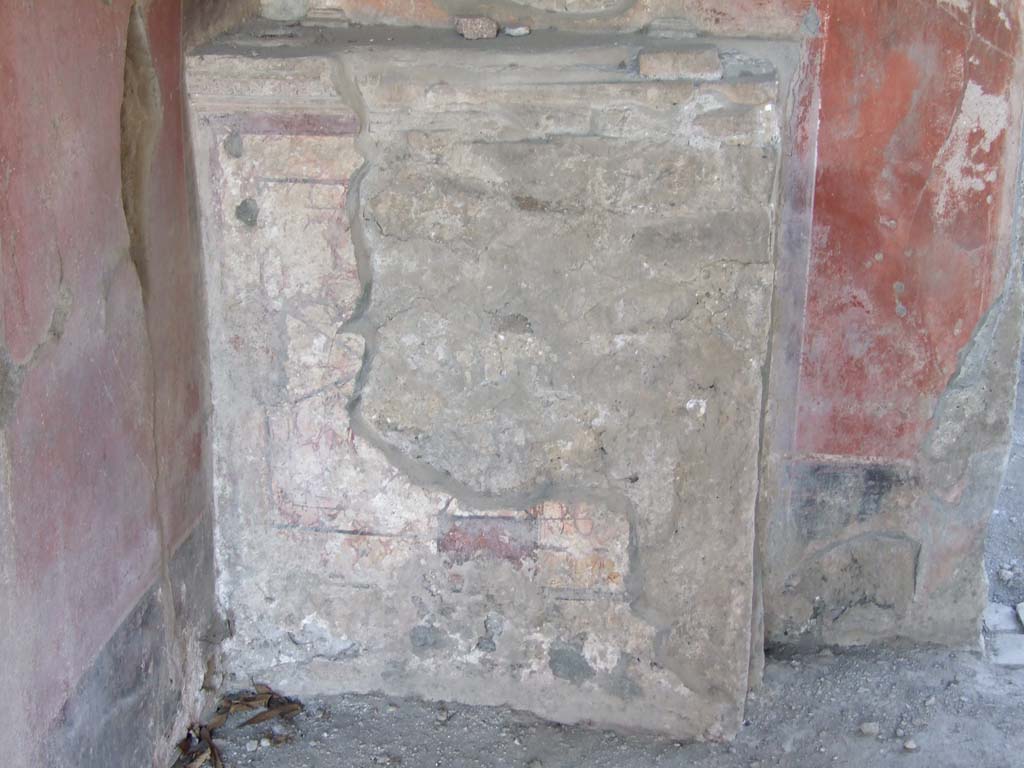 V.3.4 Pompeii. March 2009. Podium base of lararium. The podium was covered in stucco painted to look like red marble with insets.
The insets were of red rectangles and yellow diamonds with a large green slab in the centre of the two free sides. 
The slab on the south side was circular whilst that on the east was diamond shaped.
A stucco cornice in red, white and blue runs along the top of the base.
See Boyce G. K., 1937. Corpus of the Lararia of Pompeii. Rome: MAAR 14. (p. 38, 111, Pl 38,1).