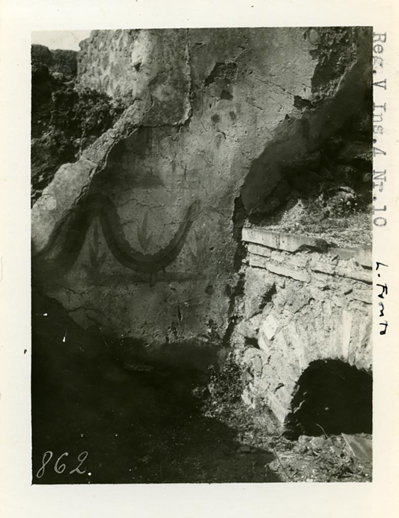 V.4.a Pompeii but shown as V.4.10 on photo. Pre-1937-39.
According to Boyce, on the west wall of the kitchen entered from the north-west corner of the peristyle, was a fragmentary Lararium painting.
One figure of a Lar was preserved, as well as the Genius pouring a libation, a Camillus, and below one red and yellow serpent advancing to the right.
A second and smaller picture had been subsequently painted over the top of that one, but only one Lar remained of that one too.
On the south wall, to the left of the entrance, was painted a ham.
See Boyce G. K., 1937. Corpus of the Lararia of Pompeii. Rome: MAAR 14. (p.42, no.128) 
Photo courtesy of American Academy in Rome, Photographic Archive. Warsher collection no. 862.