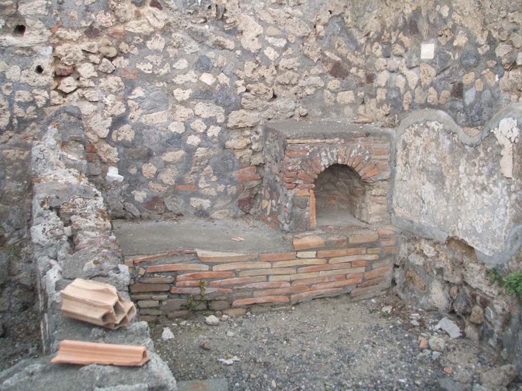 VI.7.7 Pompeii. December 2005. Kitchen, with bench and hearth against the west wall.
According to Boyce, on the north wall of the kitchen was a lararium painting.
Only a fragment was preserved, painted on a white background.
In the centre was the Genius with a cornucopia and patera standing before a burning altar.
Behind him was a camillus, above and behind the altar was the figure of the tibicen.
On either side of this group stood the Lares in yellow tunic and green pallium.
Beyond the Lar on the left was a small popa pushing a hog towards the right.
The corresponding figure on the right of the right Lar was missing, as was the whole outer section of the plaster on this side.
In the lower zone was the customary altar with the two serpents.
See Boyce G. K., 1937. Corpus of the Lararia of Pompeii. Rome: MAAR 14. (p.47, no.163)
Boyce added a note that said Helbig (58) wrongly assigned this shrine to VI.7.9.
See Helbig, W., 1868. Wandgemälde der vom Vesuv verschütteten Städte Campaniens. Leipzig: Breitkopf und Härtel. (58).
