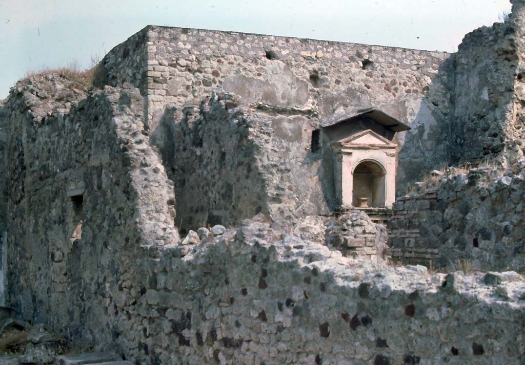 VI.12.2 Pompeii. August 1976. Looking towards north wall of kitchen, with arched aedicula niche.
Looking east over wall from first (middle) peristyle, into corridor with doorway to kitchen.
Photo courtesy of Rick Bauer, from Dr George Fay’s slides collection.