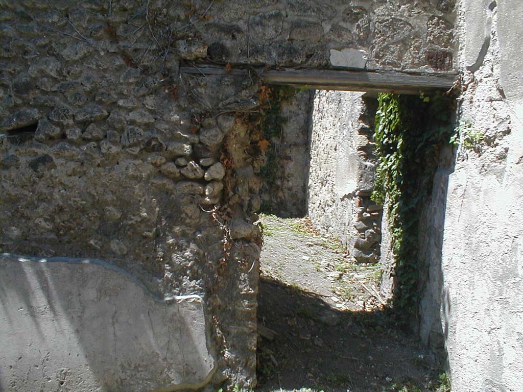 VI.15.11 Pompeii. May 2005. West wall of shop, with doorway into rear room. The rear room was linked to the atrium of VI.15.12.
According to Boyce, on the east wall in the room behind the shop, was a very crude lararium painting.
See Boyce G. K., 1937. Corpus of the Lararia of Pompeii. Rome: MAAR 14. (p.55, no.217, and Pl.22, 2).
