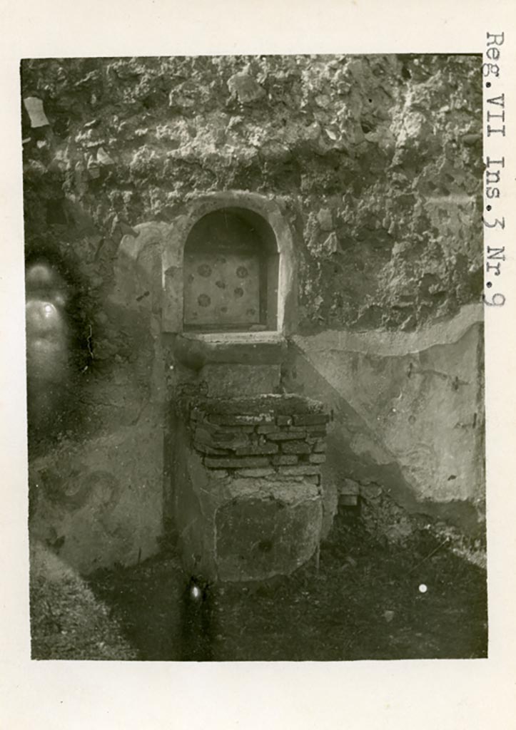 VII.3.8 Pompeii but shown as VII.3.9 on photo. 
1930s photo by Tatiana Warscher. Room “c”, west wall. Lararium and altar.
Photo courtesy of American Academy in Rome, Photographic Archive. Warsher collection no. 587.
According to Boyce –
“Against the W. wall of the central room of the dwelling quarters stands a masonry altar (0.45 by 0.50, h. 0.75), coated with yellow stucco and having the two serpents painted on the wall, one on each side of it. In the wall above the altar is an arched niche (h. 0.54, w. 0,47, d. 0.17, b. above the floor 1.0), its inside walls coated with red stucco, upon which the attributes of Hercules - a club and a skyphos twined with laurel - are reported to have been painted. The niche today shows a coating with white stucco bordered with red stripes, and upon it are painted realistic red roses. On the wall above the niche was the ordinary lararium painting of the Genius in white toga with cornucopia and patera and on each side of him a Lar. The background was richly decorated throughout: in the upper panel beside the Lares were plants and birds, on the interior of the niche were red roses, around the serpents were plants and flowers. A small panel between the top of the altar and the ledge projecting below the niche was painted in imitation of coloured marble.
Fiorelli states in the Scavi that the niche perhaps contained a statuette of Hercules, in the Descr. that it did contain such a statuette; the report in the Bull. Inst. mentions no statuette.
See Boyce G. K., 1937. Corpus of the Lararia of Pompeii. Rome: MAAR 14. (p.63-4, Pl.12,1).