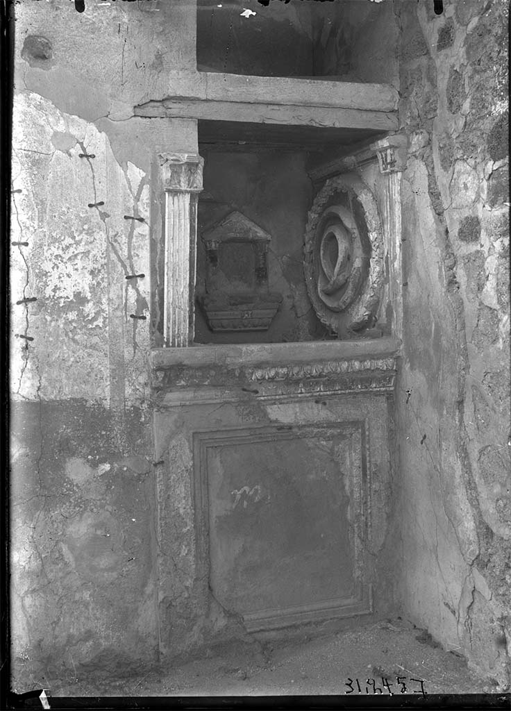 VII.3.13 Pompeii. Lararium on north wall of garden.
DAIR 31.2457. Photo © Deutsches Archäologisches Institut, Abteilung Rom, Arkiv. 
According to Boyce, in the N. wall of the viridarium, to the left of the entrance door, a deep, square niche (0.84 square, d. 0,82, h. above the floor 1.15) is set in the wall.
Its floor projects slightly in the form of a ledge and beneath it runs a delicate cornice of modelled and painted stucco. 
On the wall below the niche a rectangular panel is marked off by a moulding which runs around all four sides. 
The side walls of the niche are adorned at their outer edges, each with a stucco pilaster fitted with curious capitals, one higher than the other. 
In the centre of the back wall is a small aedicula facade formed by two columns (h. 0.25) which rest upon a heavy projecting ledge adorned with a cornice of stucco and support a pediment. 
The back wall within the aedicula is painted in imitation of marble. 
In this miniature shrine must have stood a statuette. 
On the right side wall of the niche is a large wreath (diam. 0.70) of laurel and within it coils a serpent, all done in stucco relief. 
Around the top of the three inside walls of the niche runs another stucco cornice. 
In the floor is a rectangular depression for offerings.
This shrine was called the "Double Lararium", because above the niche we have described there is another, similar to it in shape and size. 
But in this upper niche no traces of a cult were found and, in the absence of any real parallels to such a double shrine, it is simpler to regard the upper niche as a place of storage, comparable, perhaps, to the niches in the bases of the aediculae of the houses of Obellius Firmus and the Principe di Napoli (Nos. 67, 214).
See Boyce G. K., 1937. Corpus of the Lararia of Pompeii. Rome: MAAR 14, p. 64, no. 266, pl. 32,1.
See Giacobello, F., 2008. Larari Pompeiani: Iconografia e culto dei Lari in ambito domestico. Milano: LED Edizioni. (p.192, p. 280)