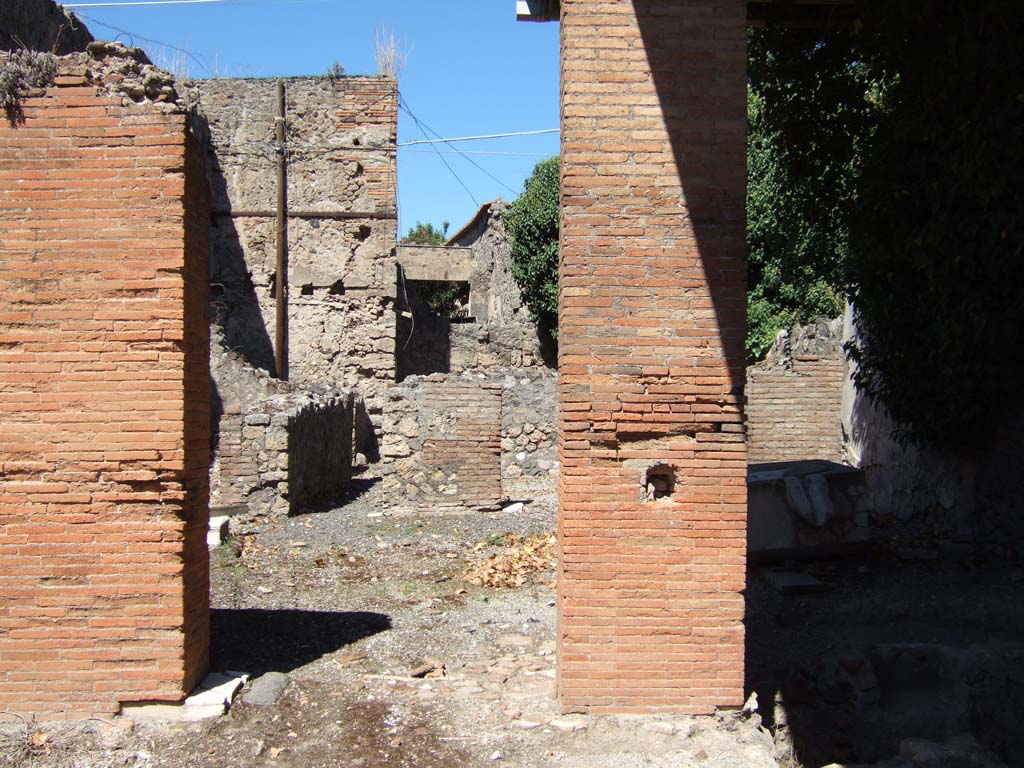 VII.4.25 Pompeii. September 2005. Doorways from VII.4.24 and VII.4.25 to rear rooms.
According to Boyce, on the west wall of the kitchen above the hearth, was a Lararium painting in two zones on a white background.
It showed the Genius pouring a libation upon an altar. On each side of him was a Lar in a blue tunic and red pallium.
Instead of the customary serpents, the lower zone was filled with a second sacrificial scene, but only the popa remains.
He held a knife in his right hand and held a hog with his left.
The hog was adorned with a red band around its belly and a garland.
See Boyce G. K., 1937. Corpus of the Lararia of Pompeii. Rome: MAAR 14.(p.65, no.272)
According to Garcia y Garcia, all the rear parts of this dwelling were damaged by the bombing in September 1943.
Demolition of the atrium, fauces and two other rooms in this area occurred, including the falling of the painted fourth style plaster.
See Garcia y Garcia, L., 2006. Danni di guerra a Pompei. Rome: L’Erma di Bretschneider. (p. 97)
According to Fröhlich, only slight faded traces of the lararium painting remain.
See Fröhlich, T., 1991. Lararien und Fassadenbilder in den Vesuvstädten. Mainz: von Zabern. (p.286, L84)