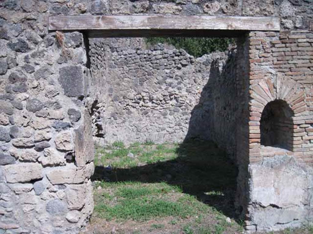 I.1.2 Pompeii. September 2010. 
Doorway to rear room "b"  in north-east corner, perhaps for the use of customers. 
Looking east. Photo courtesy of Drew Baker.
According to Warscher, quoting Mau in Bull. Inst 1875, p.26, 
“Dietro alla bottega a destra vi è la spaziosa cucina con focolare e cesso, a sinistra una stanza larga 2,96, profonda 5,24, dipinta negligentemente nello stile degli ultimi tempi di Pompei: i colori predominanti sono rosso nello zoccolo, giallo nella parte media, bianco in quella superiore.  
Sul muro di S troviamo un quadro alto 0,30, largo 0,40, rappresentante la morte di Elle.  Il fondo è tutto riempito di color turchino che rappresenta il mare. Sull’ariete che corre verso destra, sta seduto Frisso, rivolto allo spettatore e la coscia destra, come pare, coperta d’una veste bianca, tenendosi colla sinistra al collo dell’ariete, mentre stende la destra ad Elle, che dietro l’ariete affonda nel mare, alzando verso il fratello ambedue le mani.
Sul muro di E un altro quadro molto mal conservato, alto 0,38, ed altrettanto largo, ci mostra Apolline ritto in piede e rivolto a sinistra, verso la qual parte stende la man destra, mentre sopra la spalla sinistra molto svanita ma con sufficiente vertezza si scorge la lira.  La posizione elevata della lira ed il confronto delle pitture 180 e 201 (helbig) ci lasciano supporre, che essa fosse appoggiata sopra una base o un pilastro. Dal movimento del braccio destro si potrà conghietturare, che nella parte sinistra del quadro fosse ancora un’altra figura, alla quale il deo si rivolgesse”.
See Warscher T., 1936. Codex Topographicus Pompeianus: Regio I.1, I.5. Rome: DAIR, whose copyright it remains. (a, dopo no.11)
(translation:
Behind the shop to the right there was the spacious kitchen with hearth and toilet, to the left a room 2,96 wide, by 5,24 deep, carelessly painted in the style of the last days of Pompeii: the predominant colours were red on the zoccolo, yellow in the middle part, white at the top. On the south wall, a painting of the death of Helle, O,30 high, 0,40 wide, could be seen. The bottom was all filled with blue color representing the sea.
On the ram that moved to the right sat Phrixus, facing to the viewer and the right thigh, as it seemed, covered in a white robe, keeping his left hand around the neck of the ram, while extending the right hand to Helle, who behind the ram sinks into the sea, raising both hands to her brother.  On the east wall, there was another picture very poorly preserved, 0,38 high, and equally wide, showing Apollo standing and turned to the left, extending his right hand, whilst over the left shoulder, very faded but with sufficient to perceive the lyre. The elevated position of the lira and the comparison of paintings 180 and 201 (Helbig) suggested that it was placed above a base or a pillar. By the movement of his right arm, which may be conjectural that on the left side of the picture was yet another figure, to whom the god turned. The execution of both paintings as far as the bad conservation allows us to judge, seemed rather neglected, by the fact that they were overlapping onto the yellow of the wall, whether to execute a painting with greater diligence for the most, or put fresh plaster on after you finish the decorative part of the wall, or at least leave space for it."