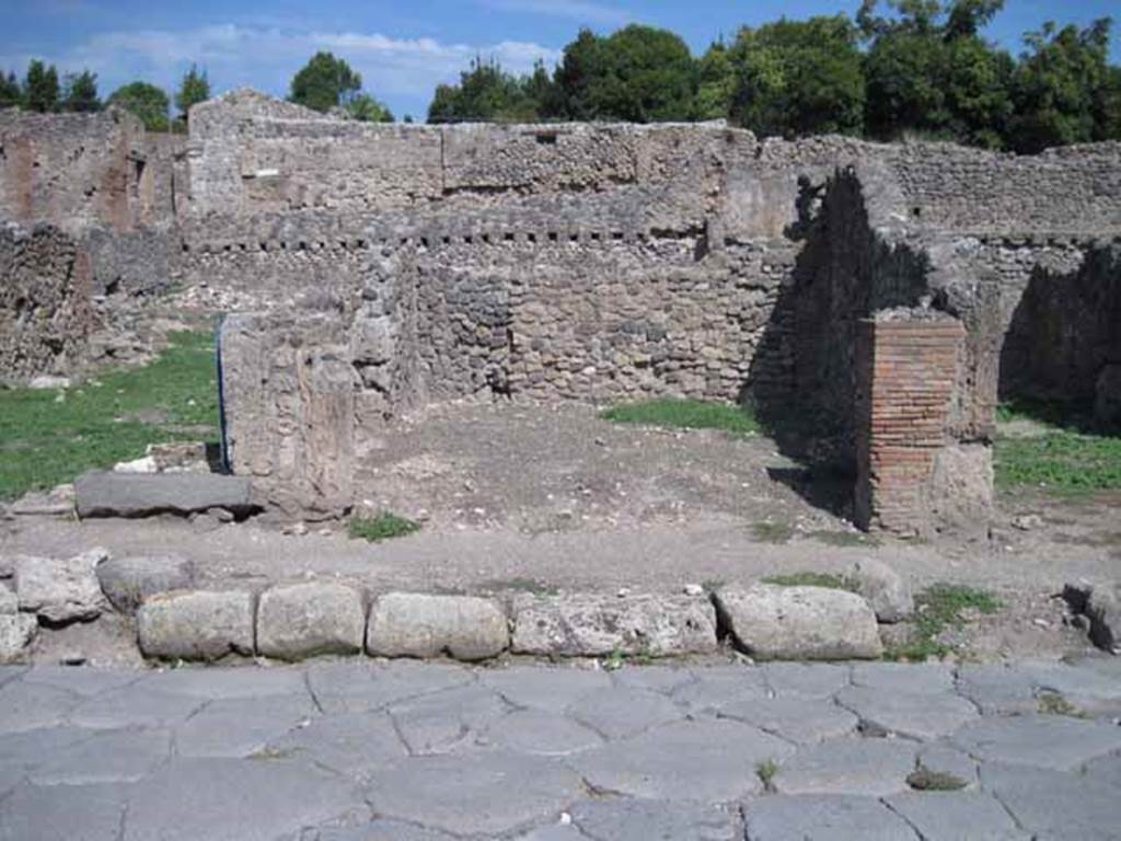 I.1.6 Pompeii. September 2010. Looking east towards entrance on Via Stabiana. Photo courtesy of Drew Baker.
According to Warscher, quoting Mau in Bull.Inst 1875, p.30, I.1.6-9:  “Segue un altro albergo, molto simile a questo descritto.  Qui pure è interrotto il marciapiede per lasciar entrare i legni. L’entrata era chiuse mediante una porta a quattro partiti, congiunti a due adue, come si conosce dai quattro buchi per i chiavistelli.  Qui pure si entra prima in un compreso che ha le dimensioni d’una bottega grande con una dietrobottega e posteriormente si apre sopra una grande corte, lungo il cui muro di fondo qui pure si stende la stalla, larga 13,30, profonda 2,47 con una finestra sul vico settentrionale e due porte, una all’estremità meridionale, l’altra poco distante da quella settentrionale. 
Presso a quest’ultima una parte della corte è selciata.   Lungo il muro N vi sono due camere con finestre sul medesimo vico, e prossimo alla stalla il cesso.  Si vede anche il cesso del piano superiore e i tubi di mattone d’un terzo, che stava ancora più in alto.  
Nell’angolo NO vi sono I primi gradini d’una scala, la cui parte superiore sarà stata di legno, in quello SO l’apertura della cisterna, e accanto nella stessa massa di materiale una vasca lunga stretta e bassa, come quella sudescritta nella casa adiacente. 
Qui la vediamo frapposto fra la cisterna ed il muro di O, il che esclude categoricamente l’aver essa servito d’abbeveratoio.  Dalla parte più bassa di essa, aperta come nella casa sudescritta, l’acqua colava in un’altra vasca larga 1,02 x 1,54, di cui un lato viene formato dalla suddetta massa di fabbrica, uno dal muro occidentale, i due rimanenti da appositi muricciuoli.   Essa ha al fondo uno scolo verso N, che dà in un vaso ossia tubo di mattone, incastrato nel suolo. Nella parete vi era la pittura dei Lari, di cui sono rimasti soltanto i serpi. A destra dell’ingresso per i legni sta un locale come una bottega. 
L’essere esso congiunto mediante una porta con quel primo compreso, ove entravano i legni, ci lascia supporre, aver esso servito di caupona per i vetturini”.
See Warscher T., 1935. Codex Topographicus Pompeianus: Regio I.1/I.5. Rome: DAIR. (no.14)
(translation: “I.1.6-9: Followed another hotel, very similar to this.  Here also the pavement was interrupted to allow entry for the “carts?”/the wood?. The entrance was closed by a door of four entries, joined two by two, as you knew from the four holes for the bolts. Here we entered first into a complex that had the dimensions of a large shop with a rear-room and behind, it opened onto a large courtyard, along whose rear wall was the stable, l3,30 wide,  2,47 deep, with a window onto the northern roadway and two doorways, one at the extreme southern end, the other not far from the north. Near to this last, a part of the courtyard was paved. Along the north wall there were two rooms with windows onto the same roadway, and the toilet was next to the stables.  Also, you could see the toilet on the upper floor and the brick pipes of a third, who was even higher still. In the north-west corner , there were the first steps of a staircase, the upper part would have been of wood, in the south-west was the opening of the cistern, and nearby in the same mass of material there was a long narrow and low basin, the same as that described in the adjacent house. Here we see it came between the cistern and the west wall, which excluded categorically that it was used as a drinking trough. From the lower part of it, open as in the described house, water strained into another large basin 1,02 x 1,54, one side of which was formed by that mass of masonry, one from the western wall, the two remaining from suitable low walls.  It had at the bottom a drain to the north, which went into a jar or brick (terracotta?) pipe, buried in the ground. On the wall there was the painting of the Lares, of which only the serpents remained. To the right of the entrance for the carts, was a room like a shop. This was connected through a door with that first area, where the carts entered,