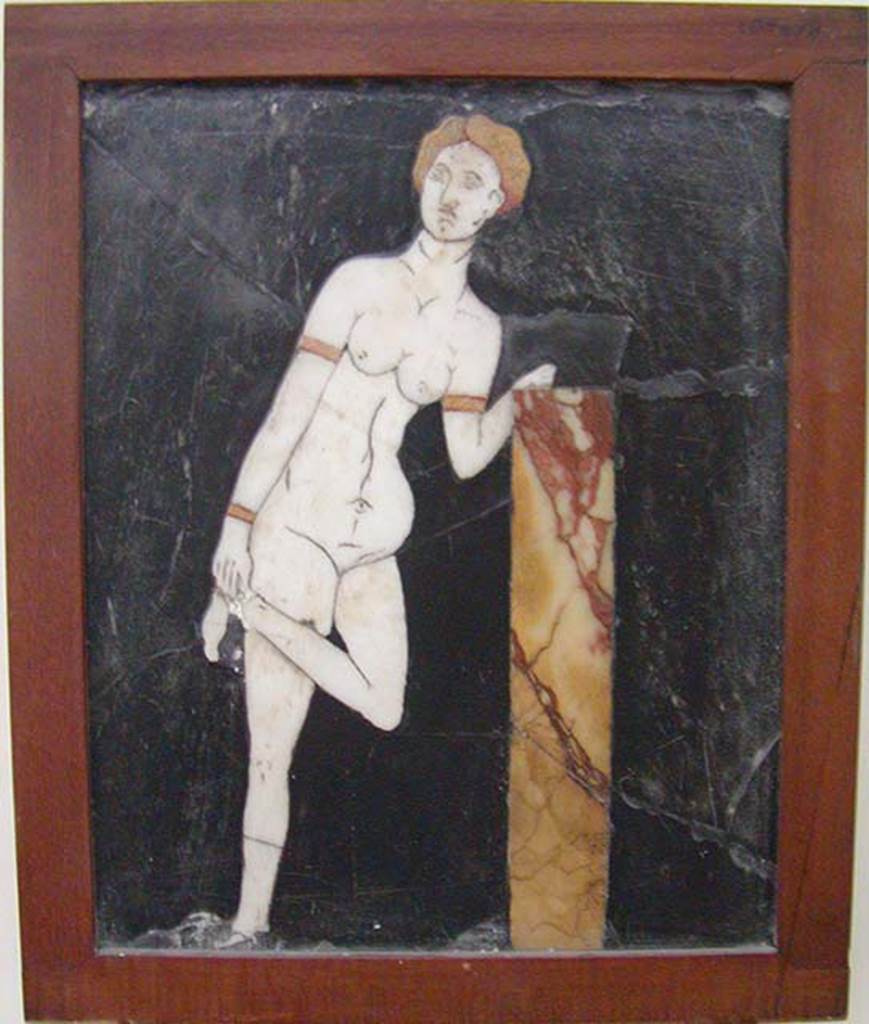 I.2.10 Pompeii. Found in triclinium. 
Black crystalline rock adorned with opus sectile tablet of Venus untying, or doing up, her sandal. 
Now in Naples Archaeological Museum.  Inventory number: 109678.
According to Fiorelli, the triclinium was adorned with paintings that were now non-existent, other than a tablet of schist inserted into the wall.
On the tablet was mounted a marble figure of Venus untying her shoes.
See Pappalardo, U., 2001. La Descrizione di Pompei per Giuseppe Fiorelli (1875). Napoli: Massa Editore. (p.35)
According to Warscher, quoting Olga Elia (Bollettino d’arte, 1929, p.276) – 
“Di due pannelli decorativi pompeiani con figure in “opus sectile” ad intarsio”
“Qui ci troviamo dinanzi ad un lavoro di ordine inferiore, di valore estetico negativo, per il rendimente del tipo e la trascuratezza della tecnica……….
Aggiungo qui un quadretto di opus sectile rinvenuto nella casa 10, of Insula 2, Regione I: vi è rappresentata su fondo nero di pietra di Genova una Venere in marmo bianco, che con capelli e braccialetti di marmo giallo, appoggiandosi con la sinistra ad un pilastrino, solleva la gamba sinistra per porsi al piede un armillo”. 
See Warscher T., 1935. Codex Topographicus Pompeianus: Regio I.2. (no.22a), Rome: DAIR.