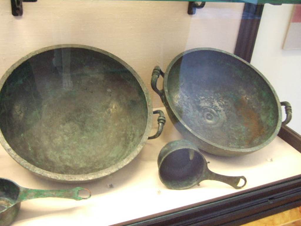 I.2.10 Pompeii.  Found in Tablinum. (left rear)  Bronze bowl.  Now in Naples Archaeological Museum. Inventory number: 111554.    (left front)  Small Bronze saucepan.  Now in Naples Archaeological Museum. Inventory number: 115975.   Found in Tablinum. (right rear)  Bronze bowl.  Now in Naples Archaeological Museum. Inventory number: 111555.  Found in Tablinum. (right front)  Small Bronze saucepan.  Now in Naples Archaeological Museum. Inventory number: 110061.